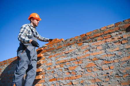 Bricklayer industrial worker installing brick masonry on exterior wall with trowel putty knife.