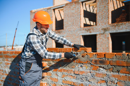 construction mason worker bricklayer installing red brick with trowel putty knife outdoors.の写真素材