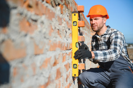 construction mason worker bricklayer installing red brick with trowel putty knife outdoors.の写真素材