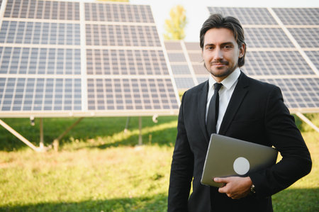 Professional engineer with laptop standing near solar panels for alternative energy in field.の写真素材