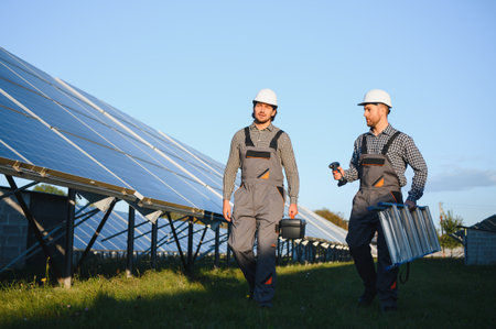 Two skilled workers or craftsmen wearing working gray uniforms, technicians are installing solar panels on a solar farm for clean energy and electricity supply.の写真素材