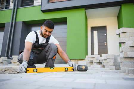Indian Worker skillfully laying paving stones using a hammer and wearing gloves, showing precision.の写真素材
