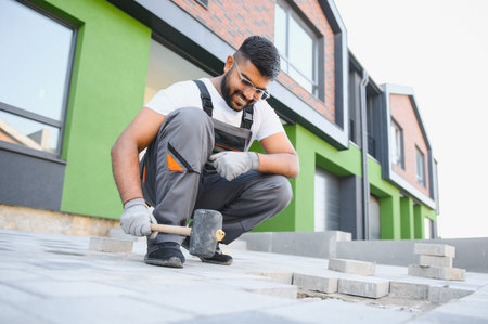 Master in gloves lays paving stones in layers. Garden brick pathway paving by professional paver worker. Laying gray concrete paving slabs in house courtyard on sand foundation base.の写真素材