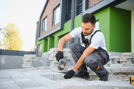 Worker skillfully laying paving stones using a hammer and wearing gloves, showcasing precision.の写真素材