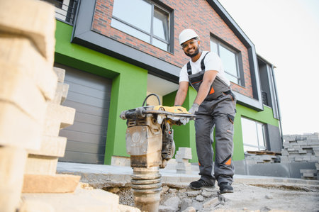 Worker using vibratory tamping machine plate compactor on a new patio driveway pavement to apply sand to fill joints.の写真素材