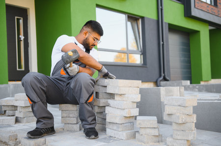 Indian Worker skillfully laying paving stones using a hammer and wearing gloves, showing precision.
