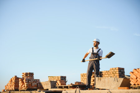 Construction worker man in work clothes and a construction helmet. Portrait of positive male builder in hardhat working at construction site.の写真素材