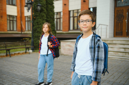 Back to school. Pupil of primary school on the way to study. Little first grader in glasses and with school bag. Beginning of lessons. First day of fall. Boy outdoors near school building.の写真素材