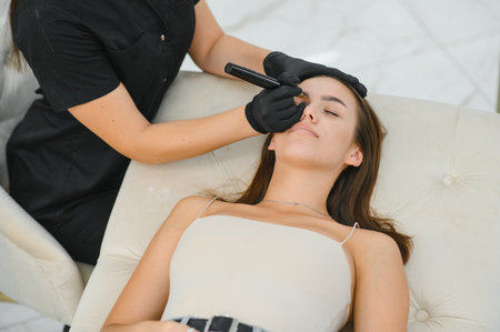 Beauty masters hands do permanent eyebrow makeup. Eyebrow microblading is performed using manipulator handle and special nozzle with needles.の写真素材