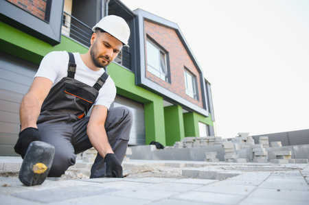 Worker skillfully laying paving stones using a hammer and wearing gloves, showcasing precision.の写真素材