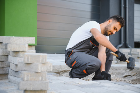 Worker skillfully laying paving stones using a hammer and wearing gloves, showcasing precision.の写真素材