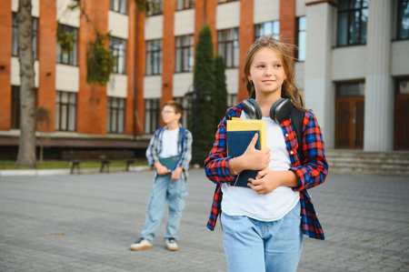 Cute girl reading a book near school. A child in the schoolyard during recess reads a school textbook. Back to school. Reading and learning in first grade.の写真素材