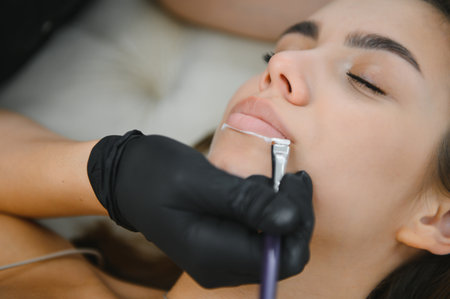 Woman With Permanent Lips Makeup at Beauty Salon During Permanent Makeup Tattoo While Drawing Contour with White Lip Pencil.の写真素材