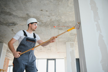 Side view of painter man painting the wall, with paint roller on big empty space. Copy space. Banner