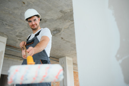 Side view of painter man painting the wall, with paint roller on big empty space. Copy space. Bannerの写真素材