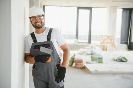 Professional worker plastering wall with putty knife indoors.
