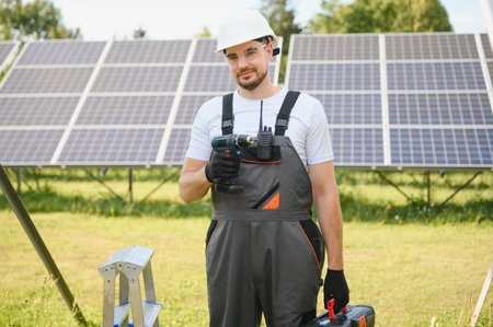 Portrait of a worker in a uniform and a white helmet with tools on a background of solar panels.