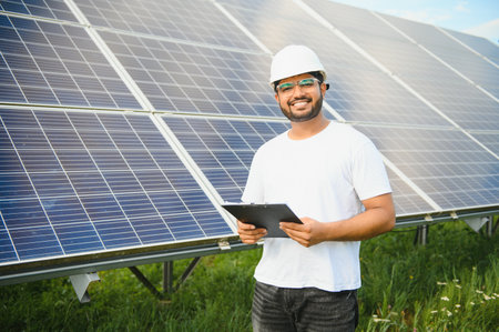 Male arab engineer standing on field with rows of solar panels.