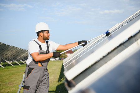 Professional Indian worker cleans solar panels with brush, green electric power technology.の写真素材