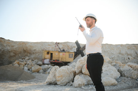A worker in a helmet stands on the background of an excavator in a quarry.の写真素材