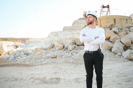 A worker in a helmet stands on the background of an excavator in a quarry.の写真素材