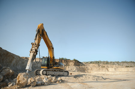 heavy organge excavator with shovel standing on hill with rocks.