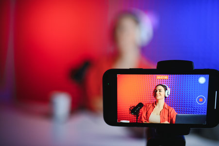 Positive trendy blogger woman speaking at smartphone webcam on tripod, recording post for vlog.の写真素材