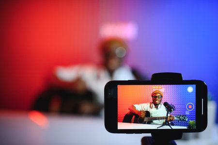 african american vlogger using smartphone to film podcast in studio. blogger with mobile phone, microphone and headphones filming video.の写真素材
