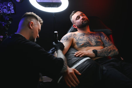 Portrait of a tattoo master showing a process of creation tattoo on a hand under the lamp light.の写真素材