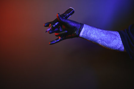 Closeup of tattooer master's hand in black glove holding machine for making tattoo art on body isolated on dark background in neon.の写真素材