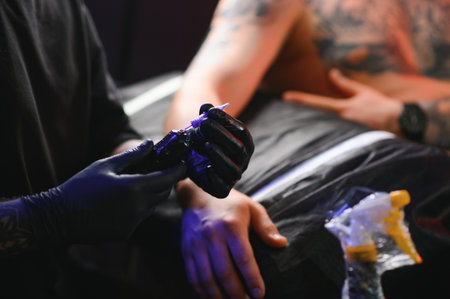 Male tattoo artist holding a tattoo gun, showing a process of making tattoos on a male tattooed model's arm.の写真素材