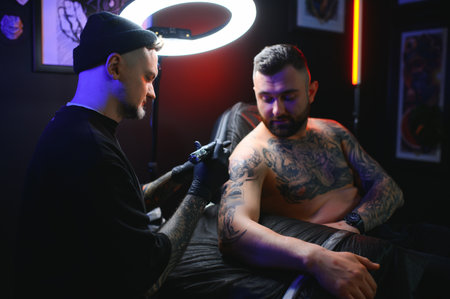 Professional tattoo artist makes a tattoo on a young man's hand.