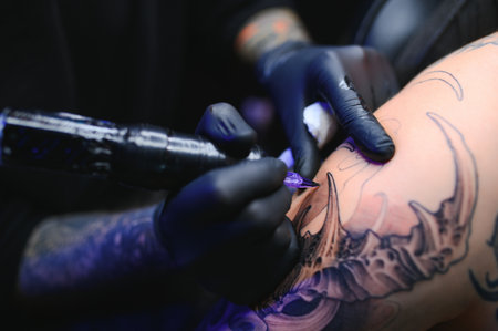 young professional tattoo master introduces black ink into the skin using a needle. Tattoo on hand.の写真素材
