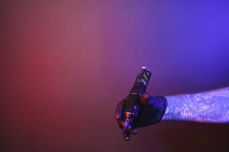 Closeup of tattooer master's hand in black glove holding machine for making tattoo art on body isolated on dark background in neon. Concept of art, job, hobby, professional equipment. Flyer for adの写真素材