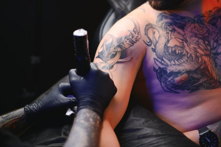 Male tattoo artist holding a tattoo gun, showing a process of making tattoos on a male tattooed model's arm.の写真素材