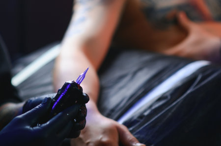 Tattoo artist hands wearing gloves and holding a tattoo machine.の写真素材