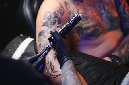 young professional tattoo master introduces black ink into the skin using a needle from a tattoo...