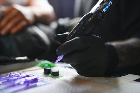 Portrait of a tattoo artist showing the process of creating a tattoo on a hand under the lamp light.の写真素材
