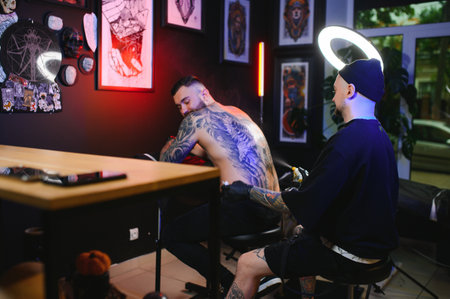 Tattoo artist man with black gloves draws a knight tattoo on the guy's back in the studio. Tattoo artist's workflow.の写真素材