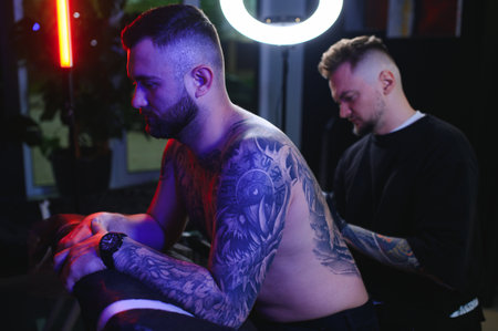 Shot of a tattoo artist and a mans back totally tattooed with black ink.の写真素材