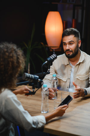 Two content creators, a man and a woman, are recording a podcast in a professional studio, engaging in conversation and using microphonesの写真素材