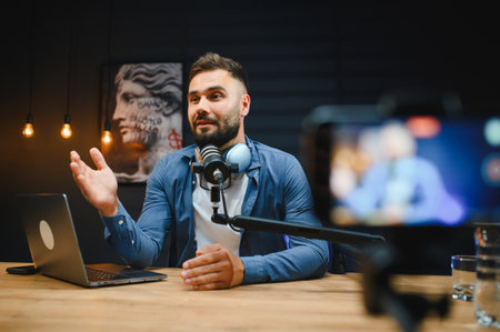 Young man engaging in podcast recording, utilizing a professional microphone and laptop within a...