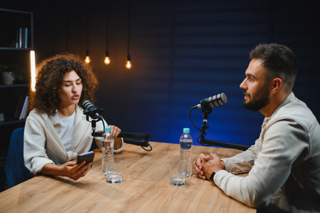 Two podcasters speaking into microphones while recording a podcast episode in a professional studio