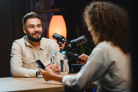 Two content creators, a man and a woman, are recording a podcast in a professional studio, engaging...