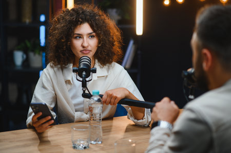 Two podcasters are recording audio content, engaging in conversation and using microphones and...