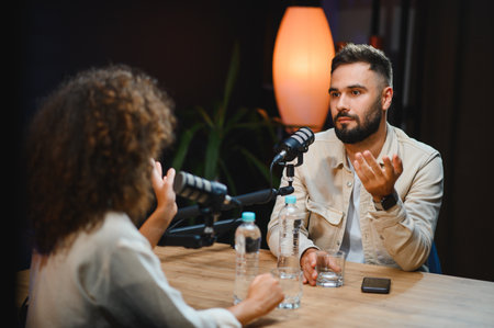 Two content creators, a man and a woman, are recording a podcast in a professional studio, engaging...