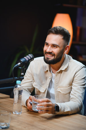 Young man smiling and holding a glass of water while recording a podcast in a professional studio