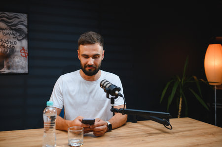 Young man using smartphone while recording audio content in home studio, creating engaging material...