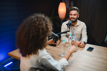 Two podcasters are recording a podcast episode in a professional studio, engaging in conversation and creating contentの写真素材