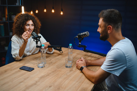 Two podcasters, a man and a woman, recording audio content in a professional studio with microphones...